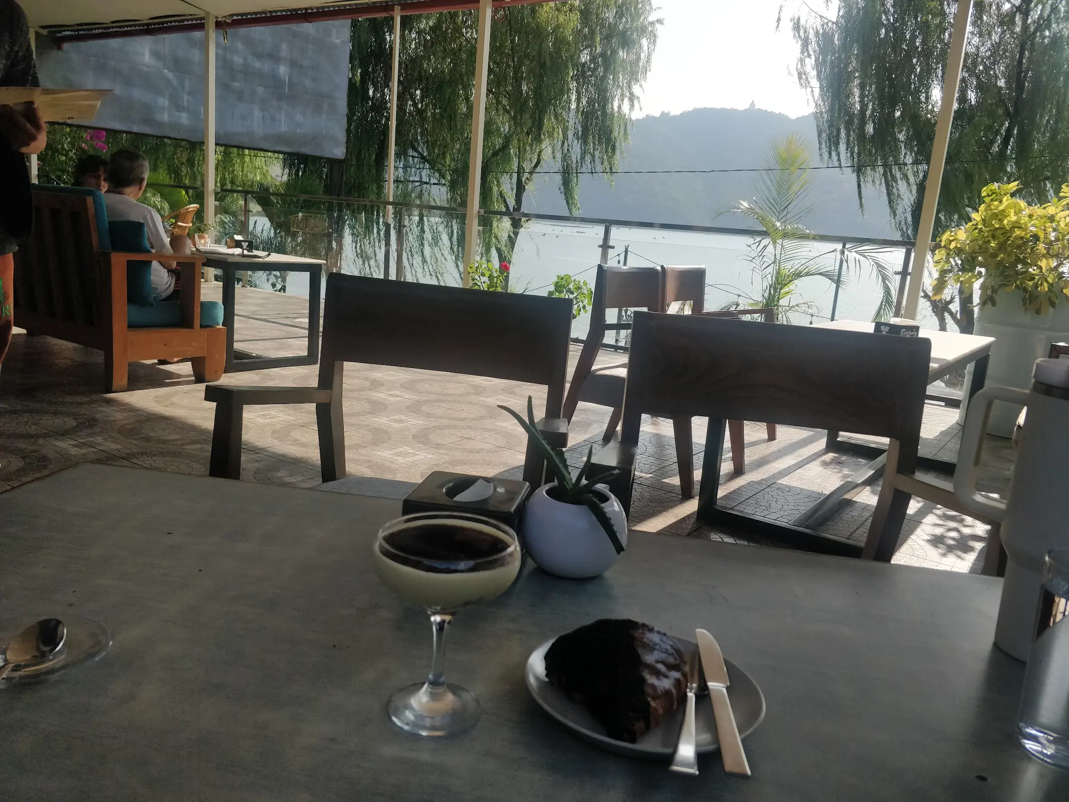 A wooden table at Amici with a chocolate dessert and espresso, the lake and willow trees visible through the window