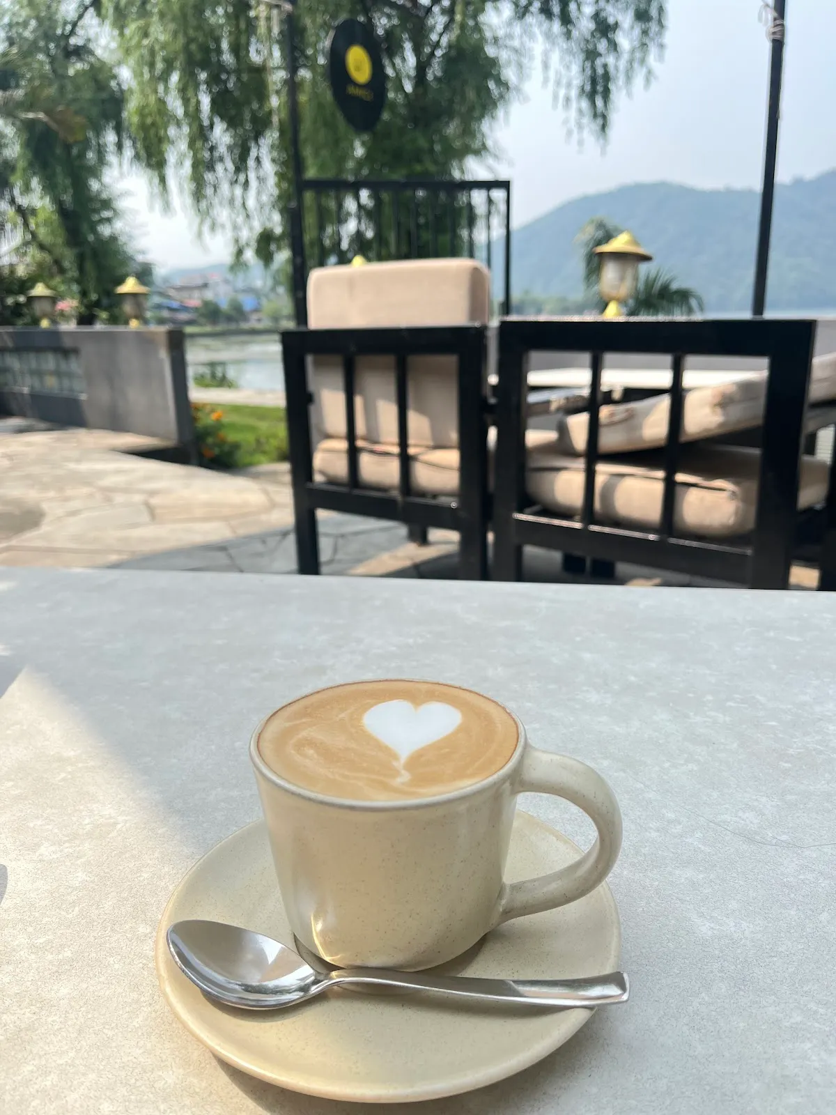 A flat white with heart latte art on a stoneware saucer, lakeside seating in the background
