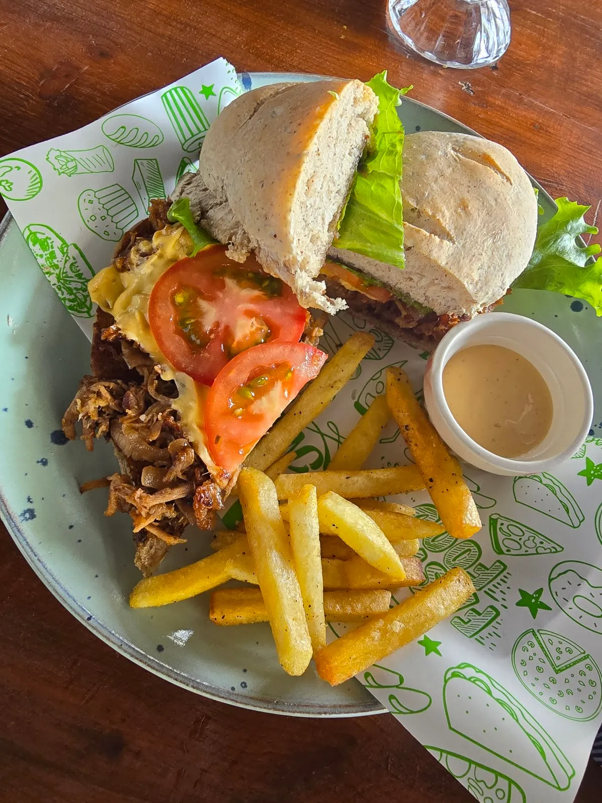 A buff burger with pulled meat, tomato and lettuce on a green-print plate with fries